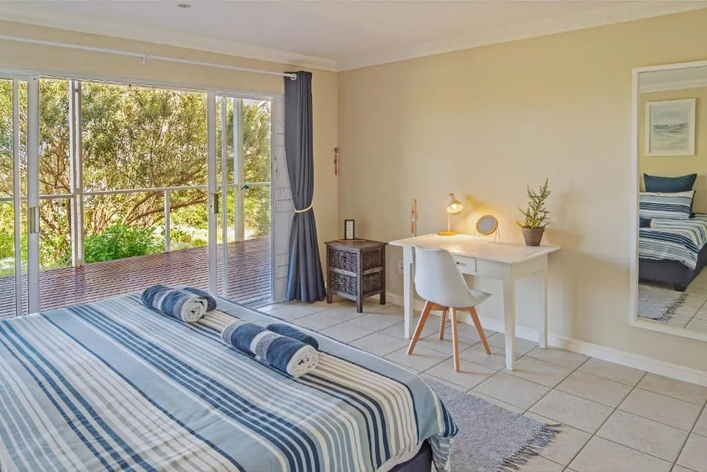 Bright bedroom with striped bedding, desk, and large sliding doors opening to deck