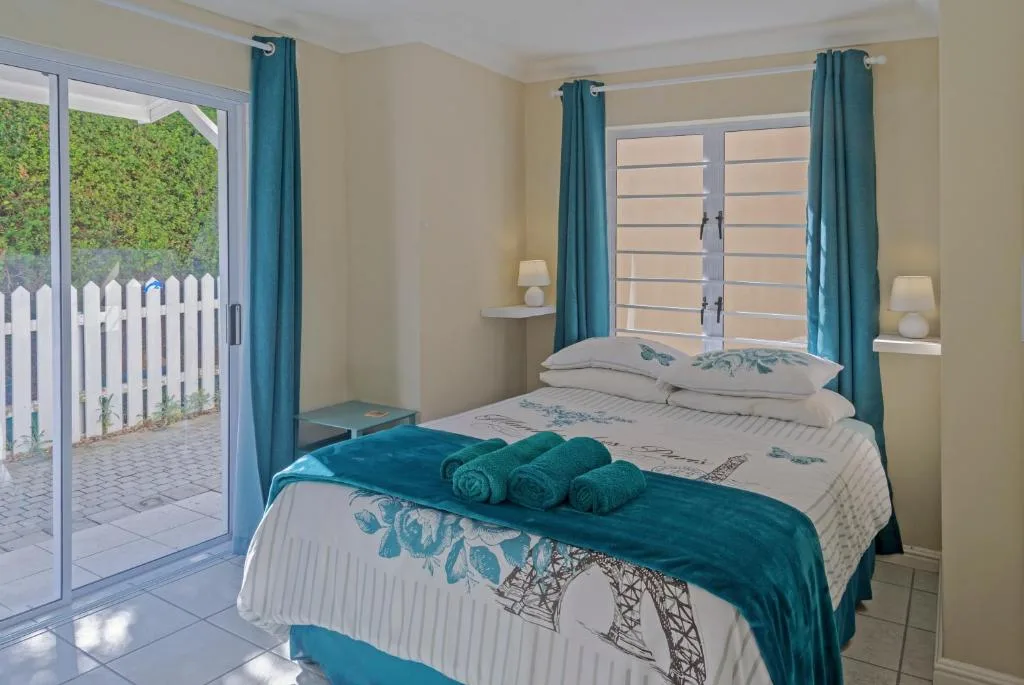 Bright bedroom with double bed, teal curtains, and direct garden access
