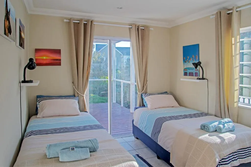 Bright bedroom with two single beds, deck access, and coastal artwork