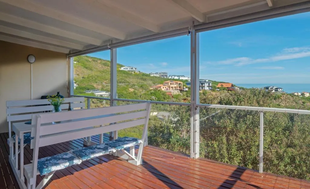 Covered deck with wooden dining table overlooking coastal hills and ocean