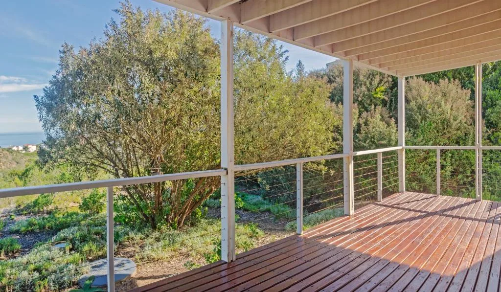 Wooden deck with glass railings overlooking lush green landscape and sea view