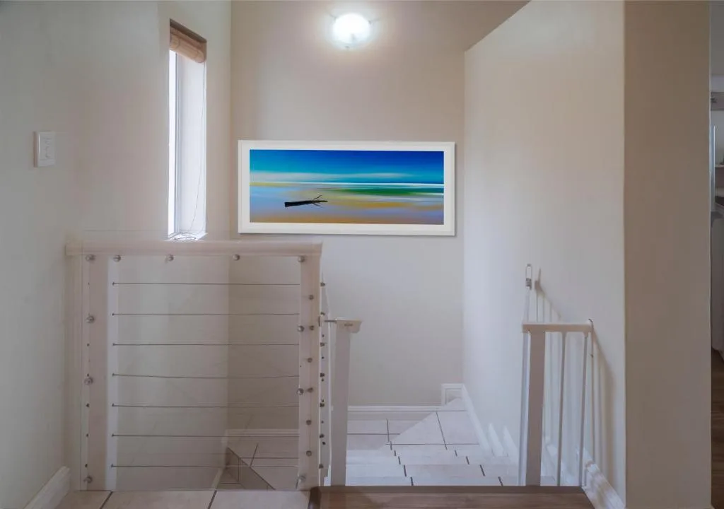 Modern staircase with white railings and coastal artwork displayed on wall
