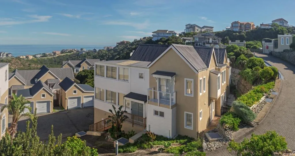 Modern coastal home with cream and yellow facade overlooking ocean and hillside gardens