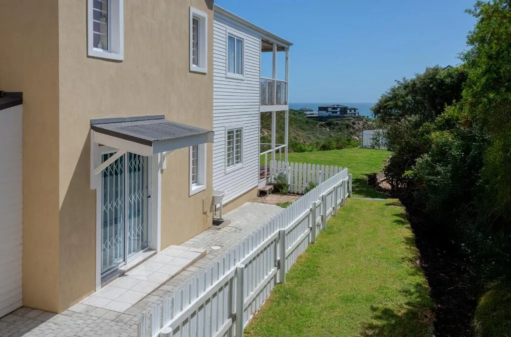 Cream and white cottage with white picket fence and ocean view in distance