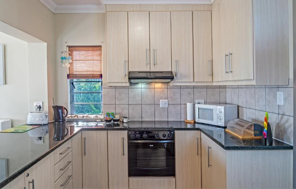 Modern kitchen with light wood cabinetry, black granite countertops, and stainless steel appliances