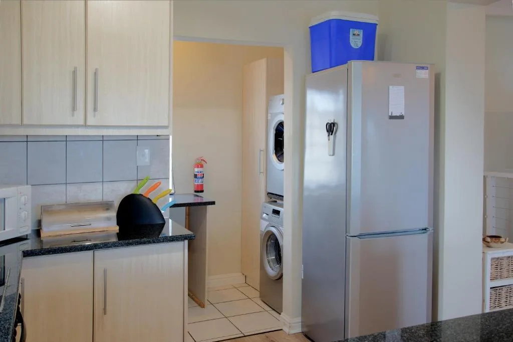 Modern kitchen with white cabinetry, stainless steel fridge, and stacked laundry appliances