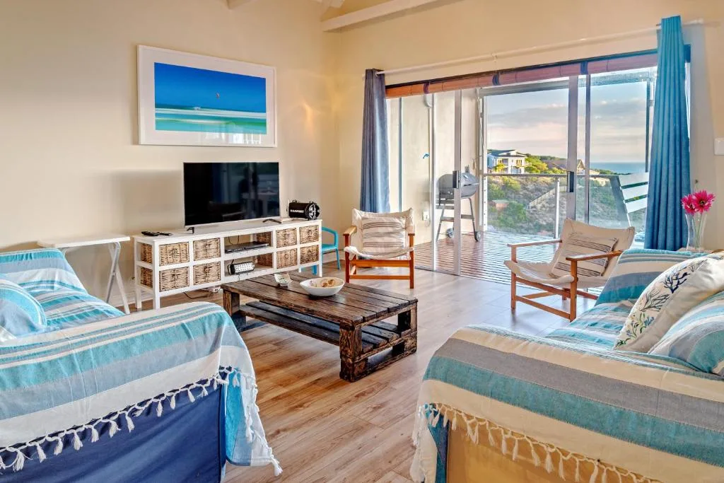 Bright lounge with coastal views, TV, comfortable seating, and ocean vista through sliding doors