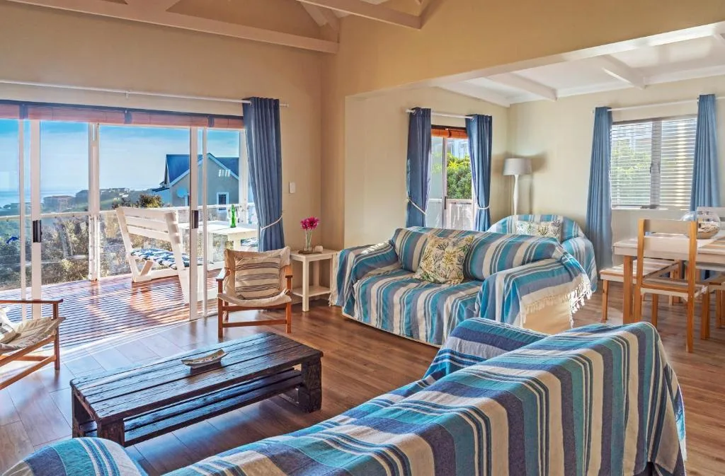 Spacious lounge with striped sofas, wooden floors, and scenic coastal views through glass doors