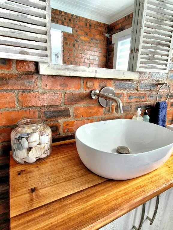 Modern white bowl sink on wooden vanity with exposed brick wall