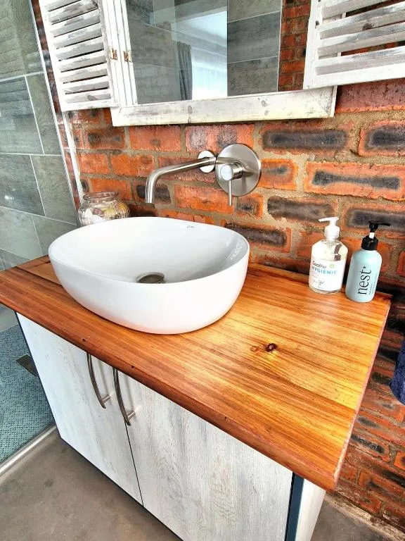 Modern white vessel sink on wooden counter with exposed brick wall