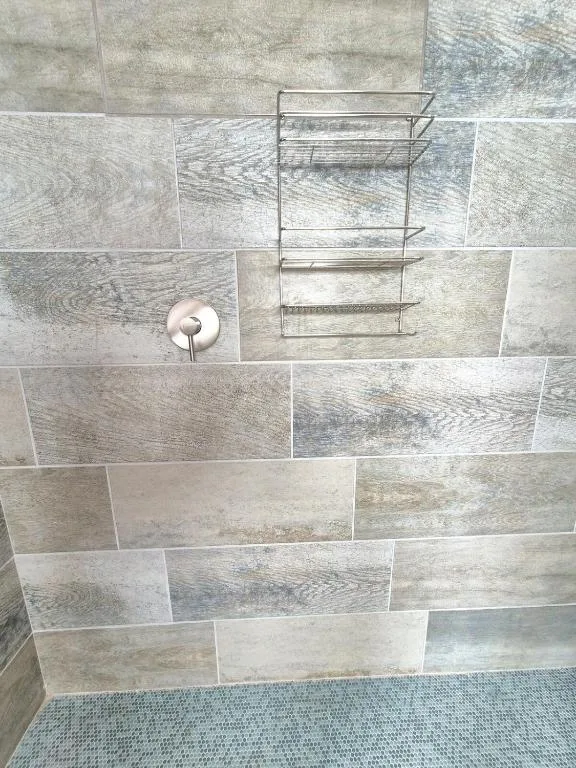 Modern bathroom shower wall with wood-grain tile and metal shelving rack