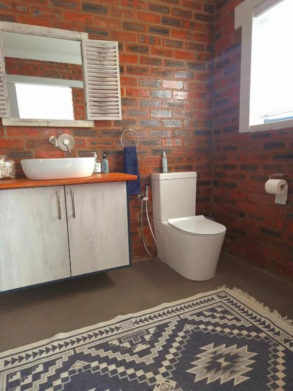 Brick bathroom with vessel sink, toilet, and patterned floor mat