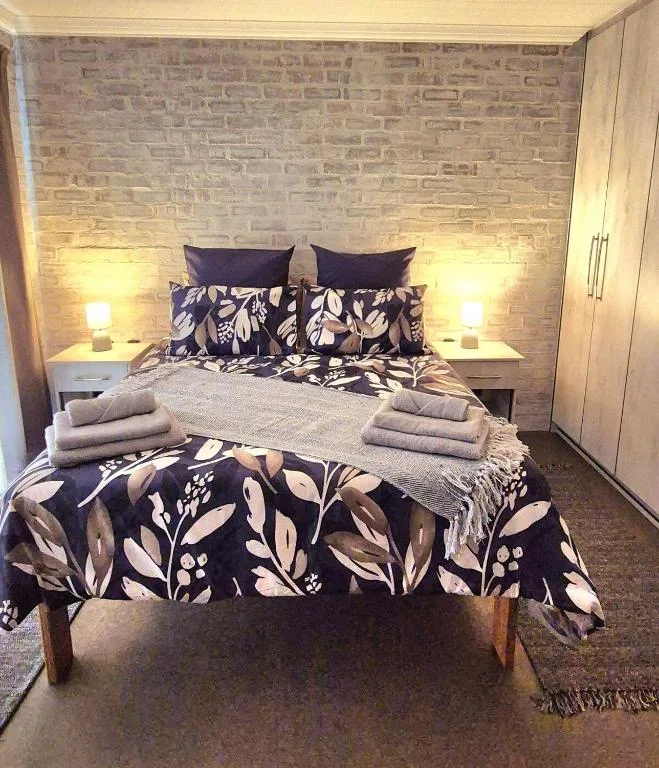 Modern bedroom with queen bed, botanical bedding, brick feature wall, and warm lighting