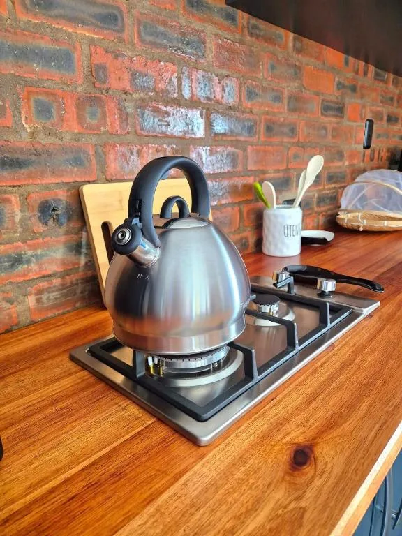 Stovetop kettle and kitchen utensils on wooden counter with brick wall