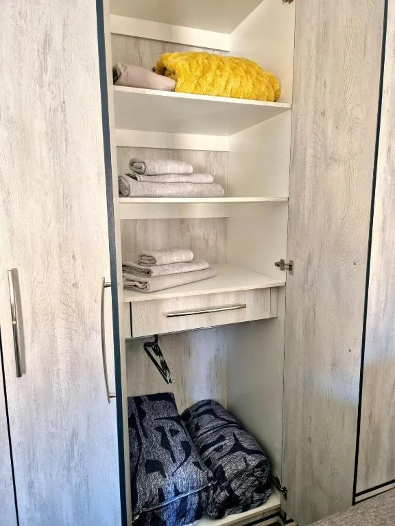 Built-in linen closet with shelves, towels, and yellow bedding
