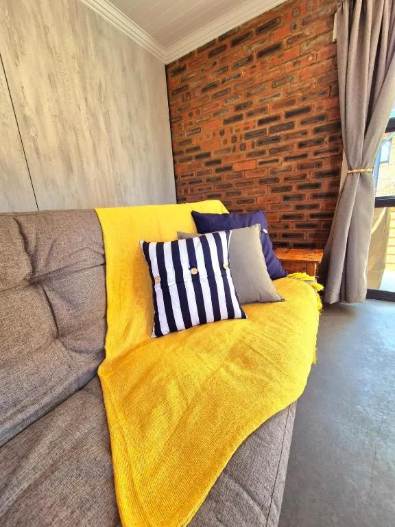 Cozy lounge with gray sofa, yellow throw, and striped pillows against exposed brick wall