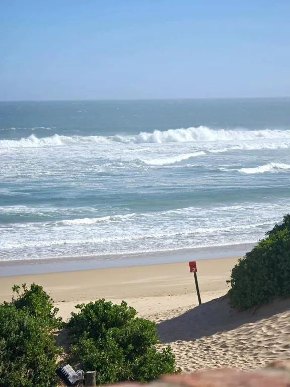 Ocean waves and sandy beach with dunes under clear blue sky