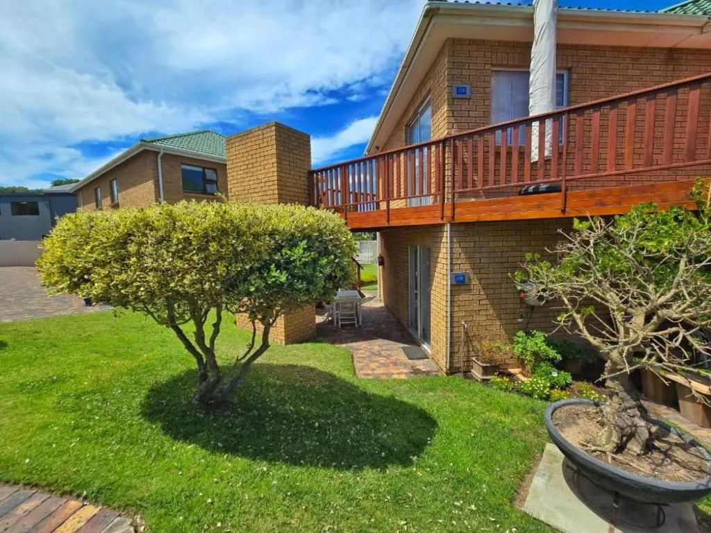 Brick home with wooden deck, manicured lawn, and mature landscaping