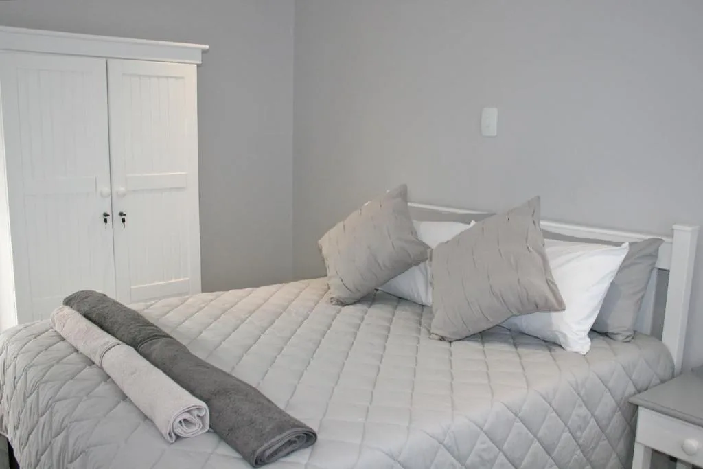 Bright bedroom with queen bed, grey pillows, and white wardrobe