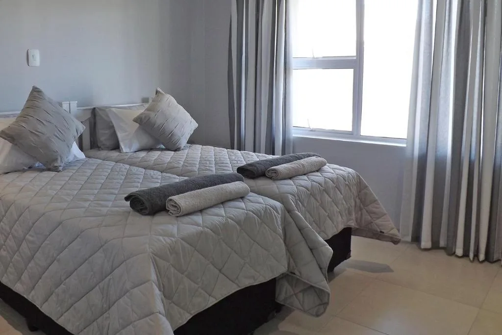 Bright bedroom with twin beds, neutral bedding, and large window overlooking garden