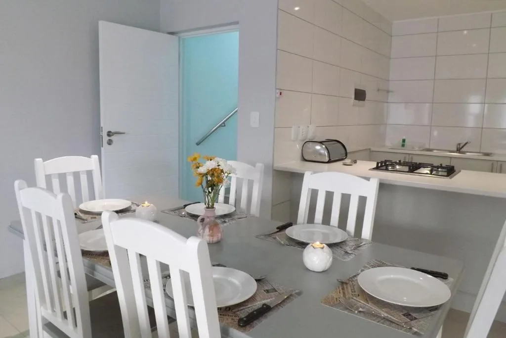 Modern dining area with white chairs and grey table, adjacent kitchen visible