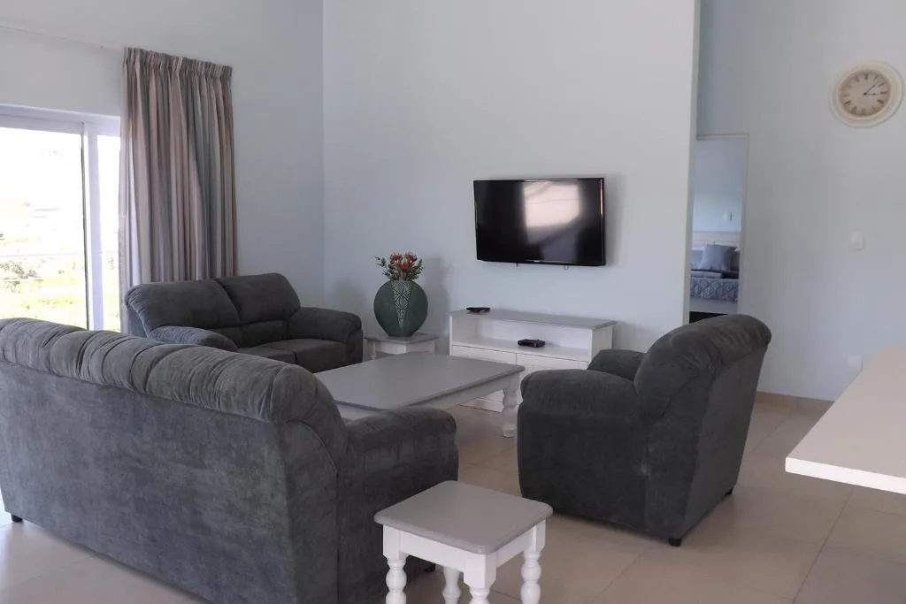 Modern lounge with dark sofas, wall-mounted TV, and bright windows