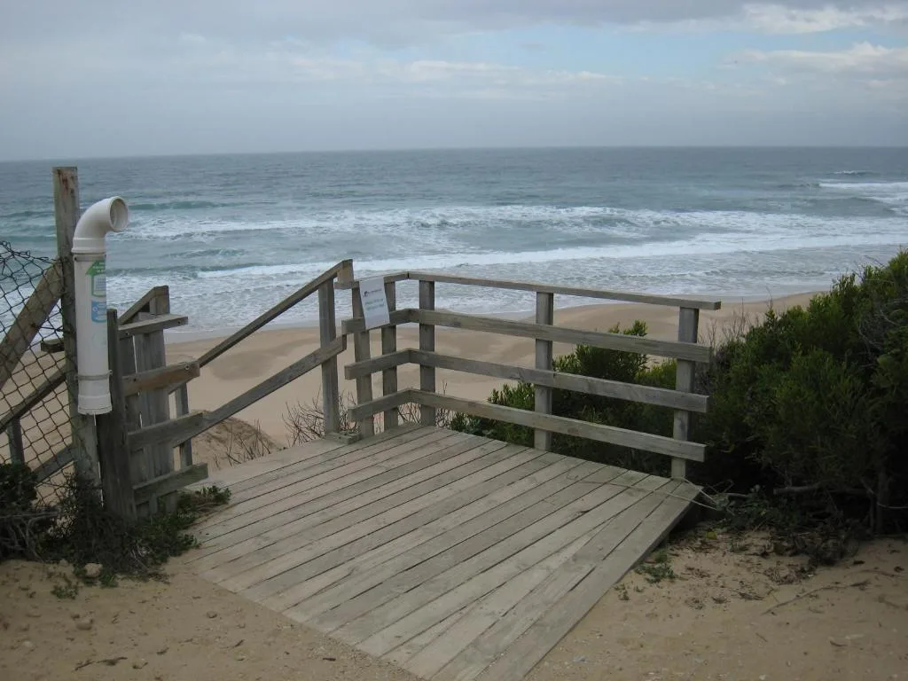 Wooden beach access deck overlooks sandy shore and ocean waves
