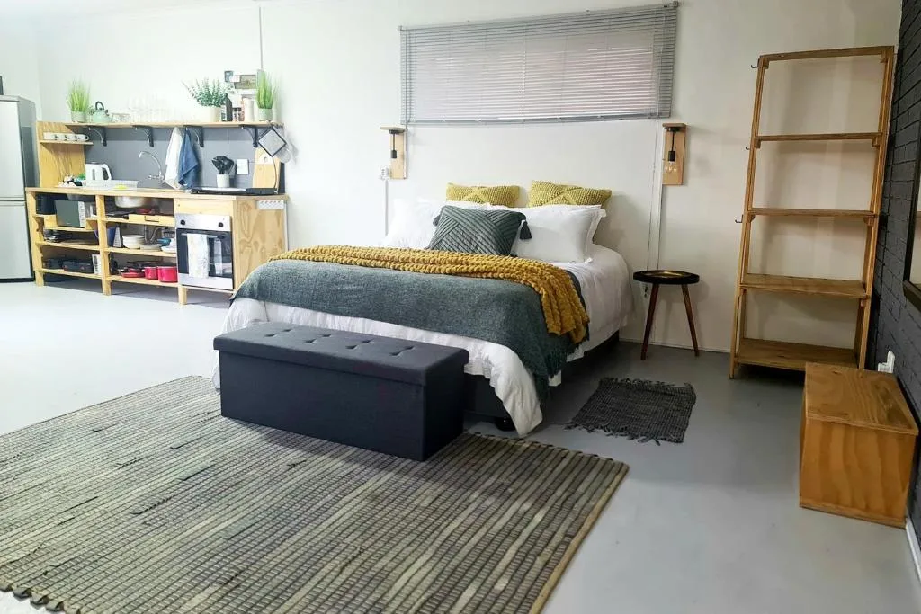 Modern bedroom with queen bed, mustard accents, storage shelving, and wooden ladder shelf