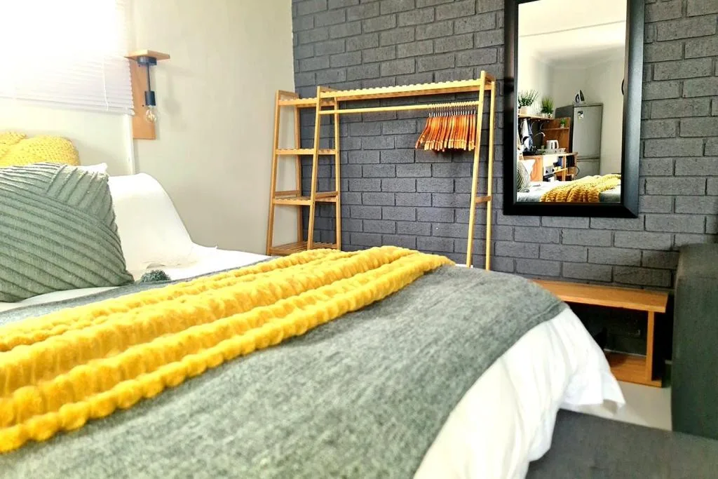 Modern bedroom with yellow bedding, wooden wardrobe, and dark brick accent wall
