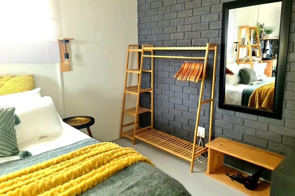 Modern bedroom with yellow bedding, wooden clothing rack, and brick accent wall
