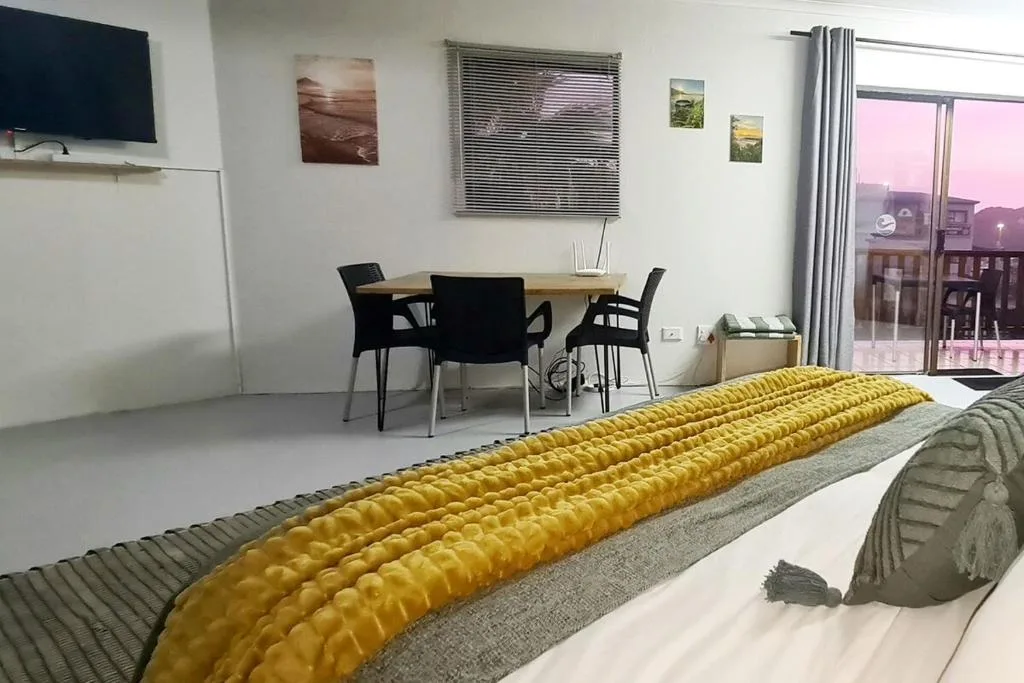 Bedroom with work desk, yellow bedding, and sunset view through large windows