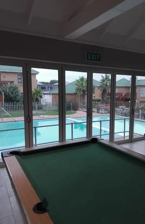 Pool table indoors with swimming pool visible through glass doors