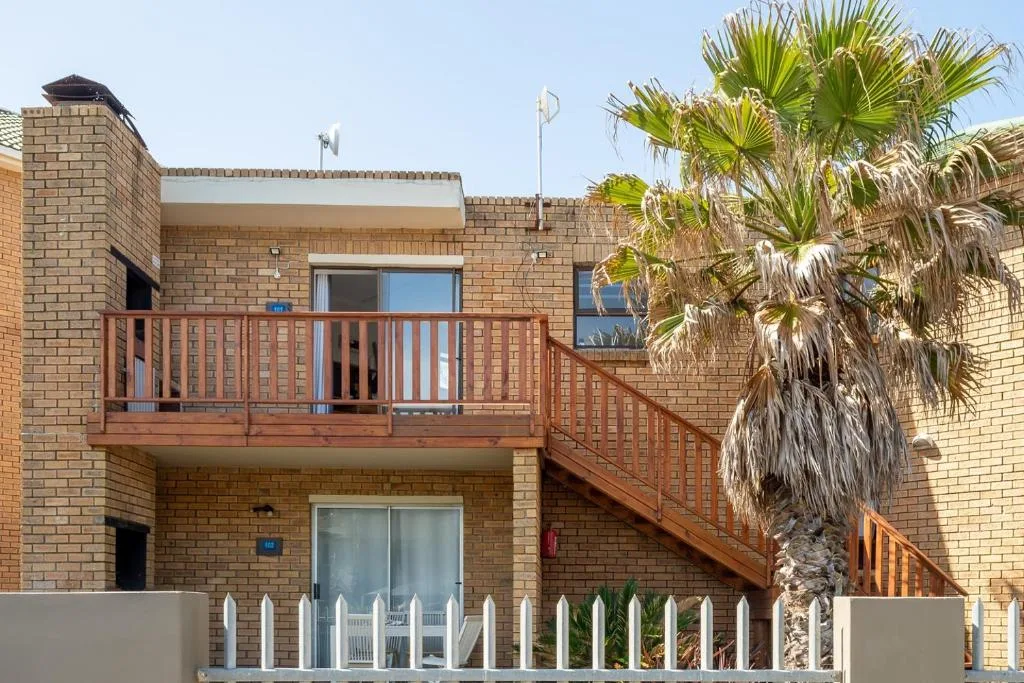Two-story brick apartment with wooden deck and palm tree landscaping