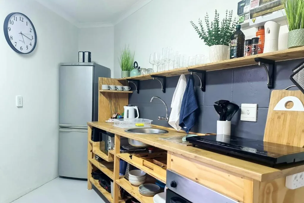 Compact kitchen with wooden counters, stainless steel fridge, and open shelving