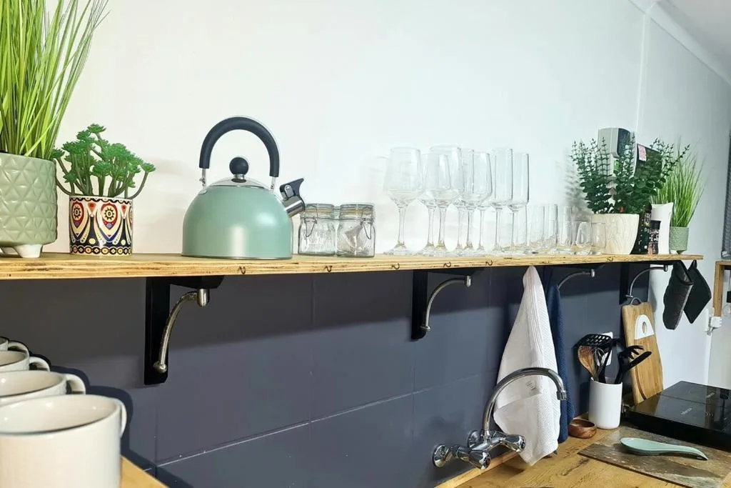 Modern kitchen counter with mint kettle, glassware, potted plants, and utensils