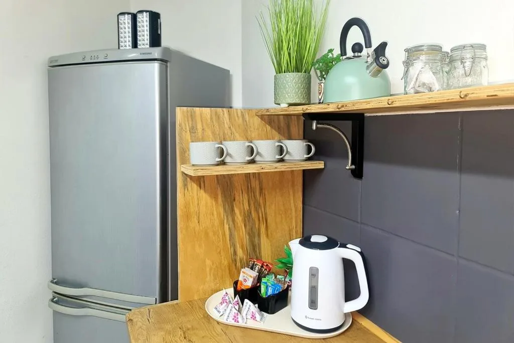 Kitchenette with stainless steel fridge, kettle, and wooden shelving