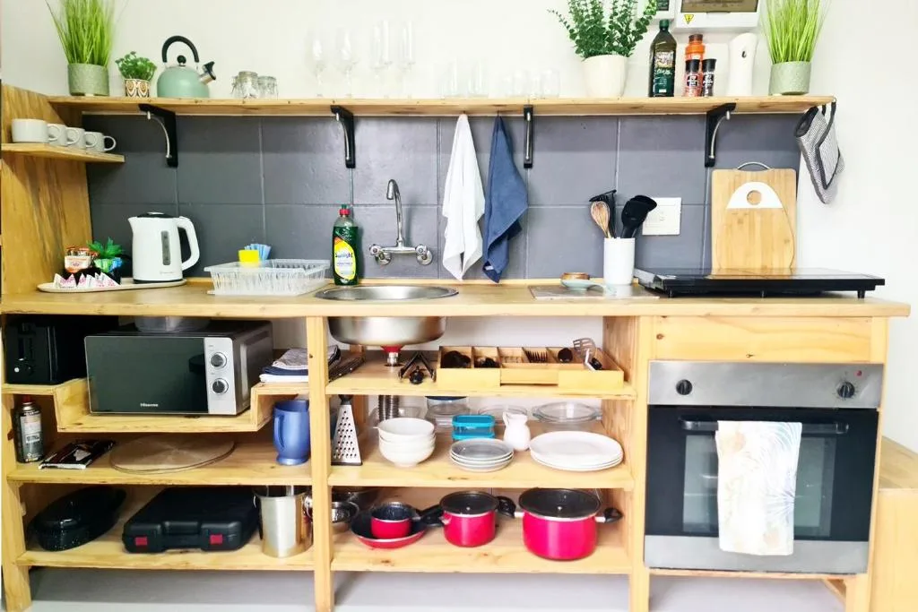 Compact kitchenette with wooden cabinetry, stove, microwave, and organized shelving