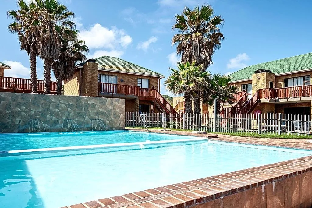 Sparkling blue swimming pool with shallow and deep sections beside brick-built holiday units