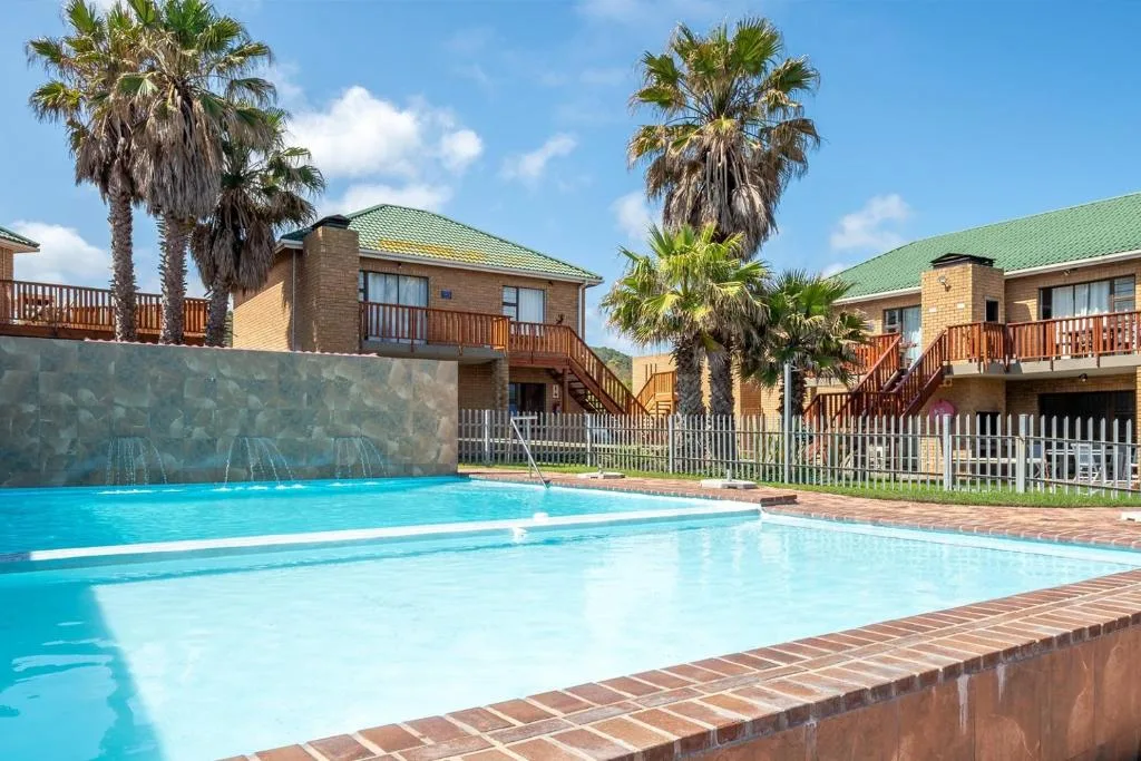 Crystal blue swimming pool with palm trees and brick accommodation units