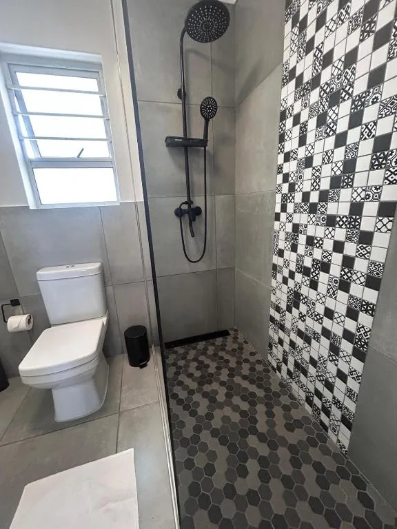 Modern bathroom with black rainfall shower, patterned tile walls, and toilet