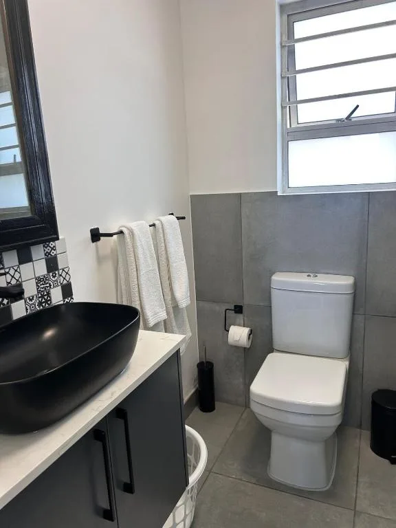 Modern bathroom with black vanity, round sink, and white toilet fixture