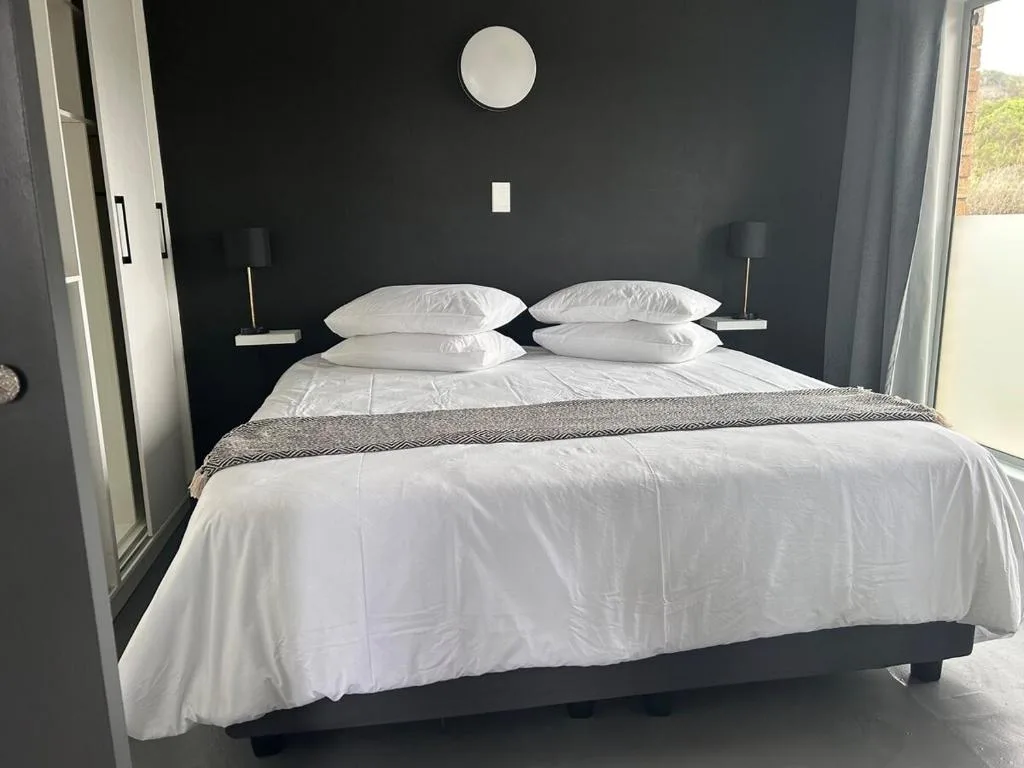 Modern bedroom with king bed, white linens, dark accent wall, and garden view