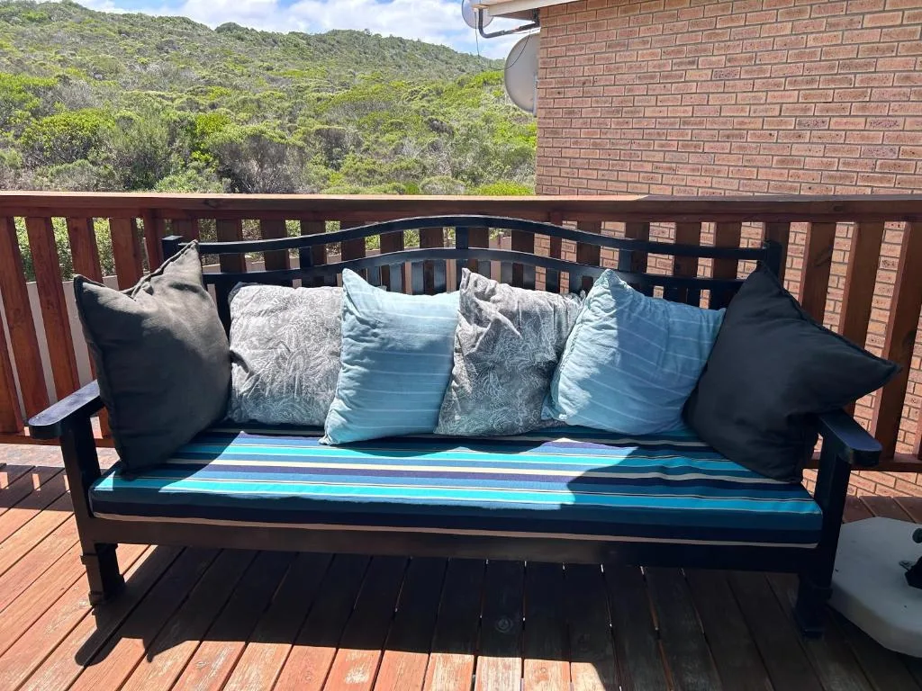 Black outdoor bench with blue cushions and pillows on wooden deck