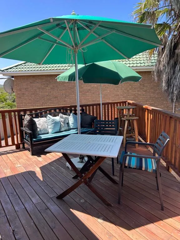 Wooden deck with dining table, cushioned bench seating, and green umbrella