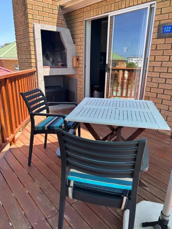 Outdoor wooden deck with dining table, chairs, and brick building facade