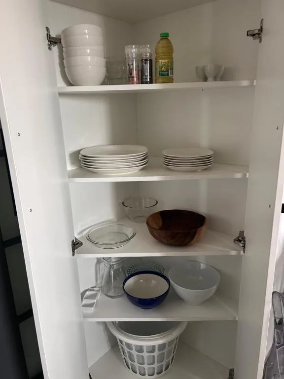 Open kitchen cabinet with white plates, bowls, glassware, and pantry items