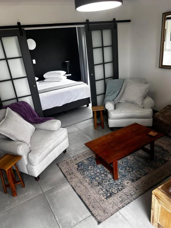 Modern lounge with cream armchairs, wooden coffee table, and open bedroom beyond