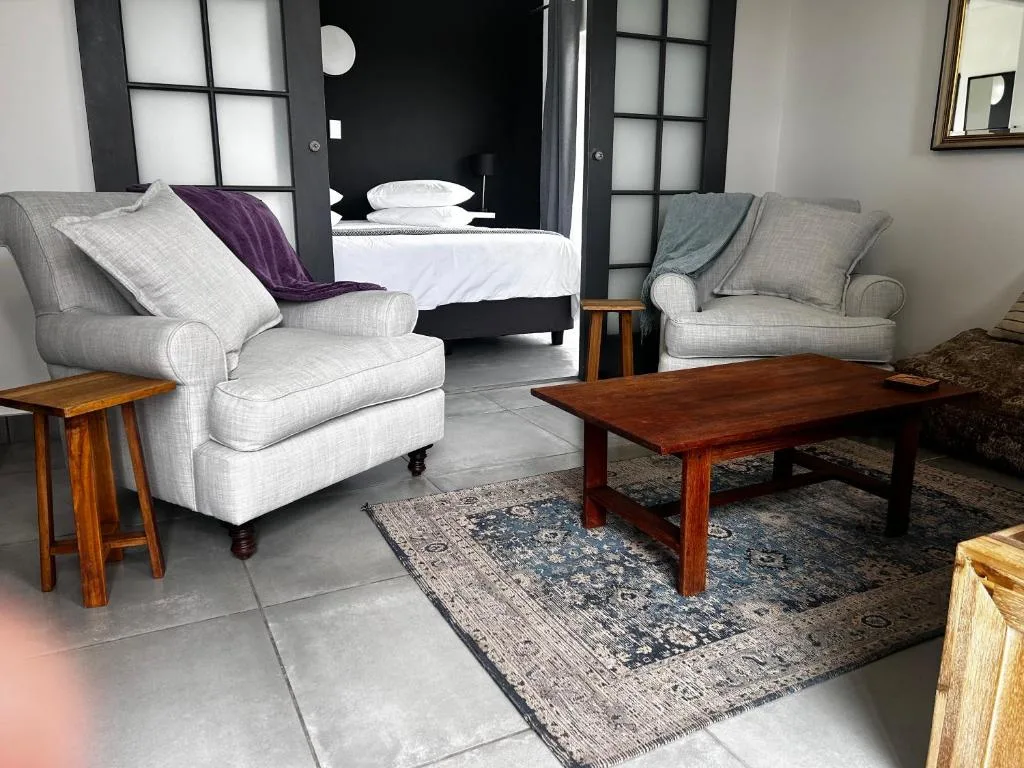 Modern lounge with cream armchairs, wooden coffee table, and bedroom visible beyond