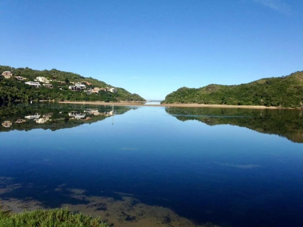 Serene lagoon view with forested hills and residential properties reflected in calm water