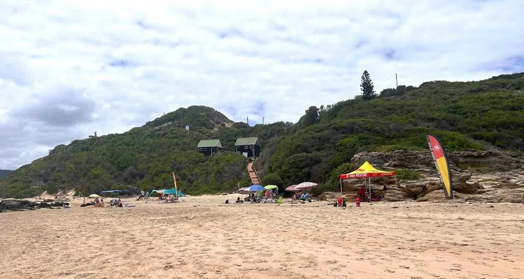 Beach access with forested hillside, sea rescue station, and coastal landscape